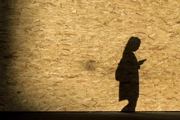 A picture taken on October 14, 2017 shows on a wooden wall the shadow of a woman looking at ther mobile phone as she walks, in Zurich. / AFP PHOTO / Fabrice COFFRINI