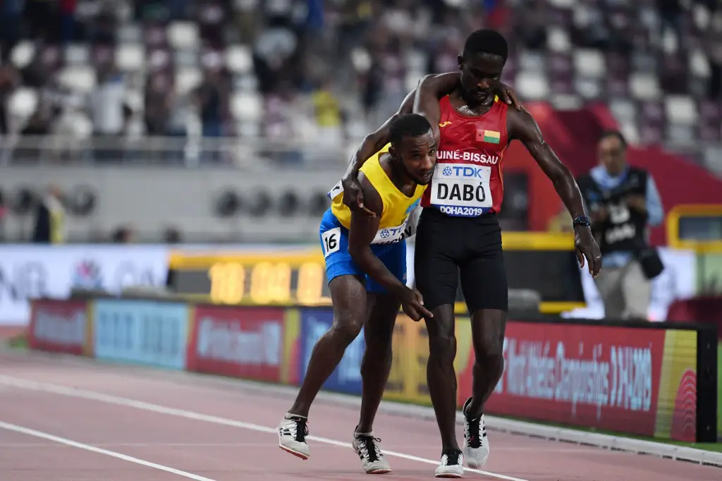 Guinea-Bissau's Braima Suncar Dabo (R) helps Aruba's Jonathan Busby to the finish line during the Men's 5000m heats at the 2019 IAAF World Athletics Championships at the Khalifa International stadium in Doha on September 27, 2019. (Photo by Jewel SAMAD / AFP)