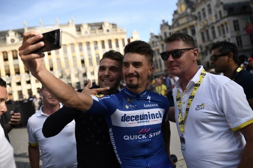 France's rider Julian Alaphilippe (C) of Belgium's Deceuninck-Quick-Step takes a selfie with his coach and cousin Franck Alaphilippe (R) and a fan during the team presentation ceremony at the Grand-Place - Grote Markt Square in Brussels on July 4, 2019, two days prior to the start of the 106th edition of the Tour de France cycling race. - On Saturday, July 6, the 106th edition of the Tour de France will start with a 194.5km stage in the region of Brussels, 100 years after the introduction of the yellow jersey and 50 years after Belgian legend Eddy Merckx won his first Tour. (Photo by Marco Bertorello / AFP)
