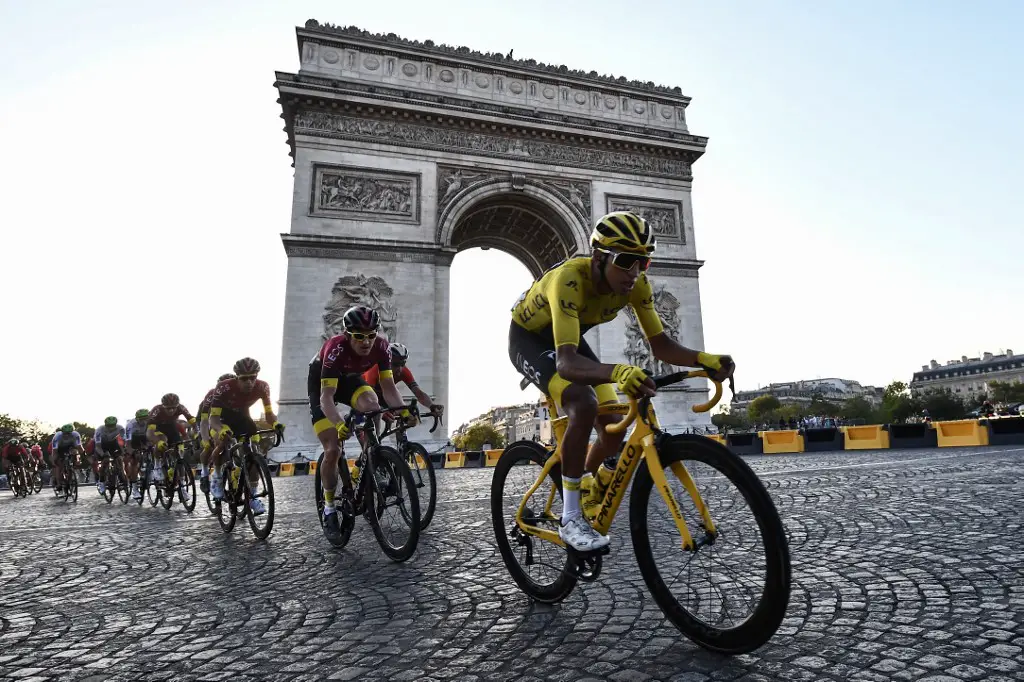 (FILES) In this file photo taken on July 28, 2019 Colombia's Egan Bernal (R), wearing the overall leader's yellow jersey (C-R) and cyclists ride down the Champs Elysees avenue next to the Arc de Triomphe during the 21st and last stage of the 106th edition of the Tour de France cycling race between Rambouillet and Paris Champs-Elysees, in Paris. - The Tour de France is not only a French monument, but also the economic heartbeat of professional cycling itself and analysts fear heavy consequences if the coronavirus crisis forces its cancellation. An announcement is expected this week on either a postponement or an outright cancellation of the 21-day extravaganza that is currently scheduled to start in Nice on June 27. (Photo by Anne-Christine POUJOULAT / AFP)