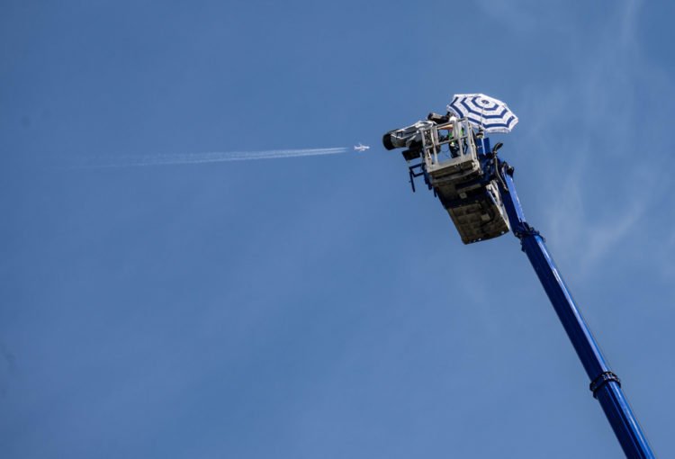 15 August 2021, Hessen, Frankfurt/Main: In calm and sunshine, a cameraman with a parasol stands at a lofty height on the platform of a mobile crane. From there he offers a television perspective of the European Triathlon Championship, the Ironman Frankfurt, which is taking place down on the Main. On the left, a commercial aircraft is flying in the blue sky above the city. Photo: Frank Rumpenhorst/dpa 
By Icon Sport - Francfort (Allemagne)