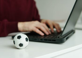 Young man reading soccer news or writing football article on laptop. Soccer ball on the table. Betting, gambling concept.