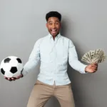 Homme africain souriant tenant un ballon de football et des billets de banque